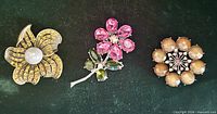 All three floral brooches displayed on dark fabric
