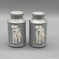 Front view of both gray ceramic shakers with cow motif