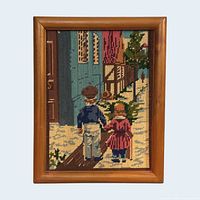 Front view of framed needlepoint showing full design of children walking in winter street scene