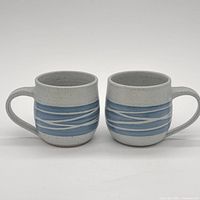 Front view of both stoneware mugs showing glaze pattern and handles