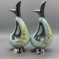 Front view of both ceramic ewers showing shape, colors, painted landscape, gold trim