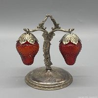Front view of pair of strawberry shakers hanging on ornate silver-plated stand
