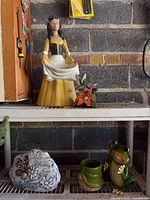 Shelf with lady statue, floral figurine, stone plaque, frog statue, green planter