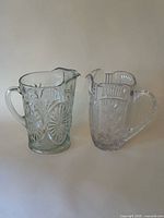 Front view of both clear cut glass pitchers side by side showing overall shapes and patterns