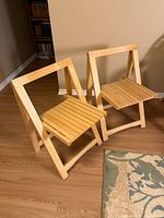 Two folding wood chairs shown open on wood floor