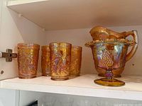 Four tumblers and pitcher with compote dish on cabinet shelf