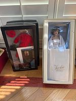 Doll boxed with white outfit next to black accessory box