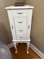 Front view of white jewelry cabinet showing drawers and legs