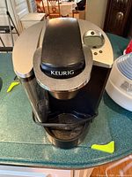 Front view of Keurig brewer showing brand badge, water reservoir, drip tray