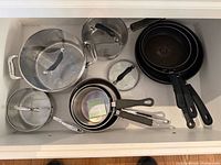 Entire lot inside drawer showing stainless pots with lids and nested non-stick frying pans