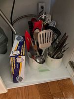 Cabinet shelf view with boxed digital kitchen scale and two utensil caddies filled with assorted utensils