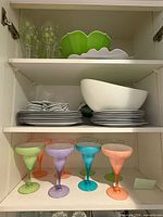 Cabinet shelves showing margarita glasses, polka-dot glasses, serving bowls, stacks of plates
