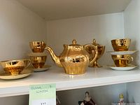 Full view of gold luster tea service on shelf: teapot, sugar bowl, four cups and saucers
