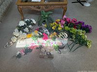 assortment of faux florals on floor with vases and potted plant