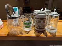 Group shot showing pitcher, printed mug, three ceramic steins and lidded cut-glass stein