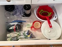Drawer view showing entire assortment: blender base, cups, colanders, apple slicer, measuring jug, mug, lid, oven mitts