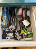 Drawer with assorted utensils including knives, ladle, tongs, can opener, corkscrew, avocado slicer