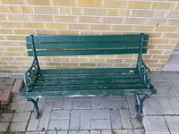 Full front view of green cast iron and wood bench against brick wall