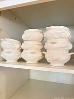 Stacked view of six of the eight white ceramic soup bowls showing molded seashell motif and side handles