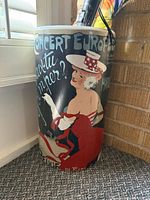 Full view of umbrella stand showing French poster graphics and cylindrical shape