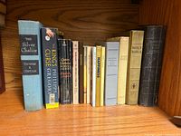 Full shelf view of 13 upright books including The Silver Chalice, The King’s Curse, Queen Victoria, Holy Bibles and others