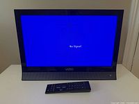 Front view of powered-on Vizio TV displaying No Signal with remote in front