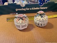 Both ceramic trinket boxes with lids in place beside tape for scale