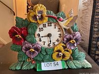 Front view of sculpted floral desk clock showing dial, pansy flowers and hummingbird