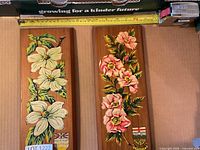 Both cedar plaques side by side showing floral motifs and shields