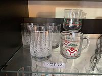 Group of Christmas themed glassware on shelf: four frosted tree tumblers, one handled mug, one stemmed goblet