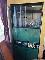 Full view of tall black and green display cabinet with glass upper section