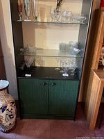 Front view of cabinet showing green base doors, black frame and glass shelves