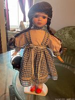 Full view of Dorothy porcelain doll on stand showing outfit, accessories and overall condition