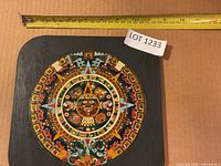 Full view of plaque showing complete Aztec calendar design with tape measure indicating size (~23 cm)