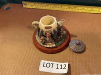 Front angled view of cottage-style miniature teapot on wood base with lid beside