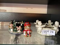 Full view of three items on shelf: caroler tealight holder, teddy bear figurine, white cherub candle holder