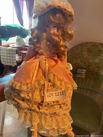 Front view of porcelain doll wearing floral lace dress with peach bow, stand partly visible