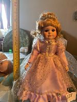 Full view of porcelain doll on stand beside ruler showing height ~14 in