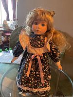 Full view of porcelain doll on stand in floral dress
