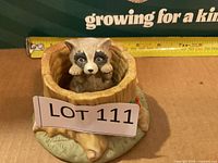 Raccoon figurine seated in tree stump base with ruler for scale