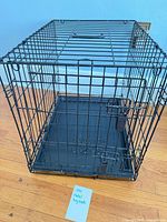 Overall view of black wire dog crate with front door closed and plastic tray inserted