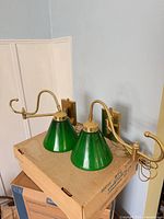 Pair of brass swing-arm sconces with green glass shades on box