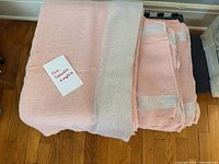 Folded pink tablecloth showing wide silver metallic border, stack of matching napkins beside