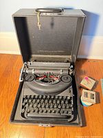 Typewriter inside open carrying case with key and ribbon boxes visible