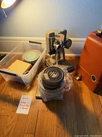Projector, case, plastic bin with film reels and stack of reel cans