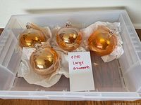 Four gold/amber iridescent glass ornaments in storage tub