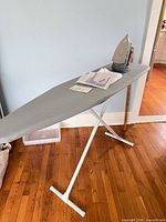 Ironing board open with iron, manuals, pressing cloth package on surface