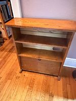 Front view of narrow oak bookshelf showing two shelves and drop-front compartment