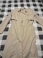 Full view of front of beige H&M coat laid flat showing overall length, sleeves, buttons, pockets