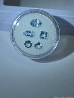 Five aquamarine gemstones in clear round case, mixed cuts visible